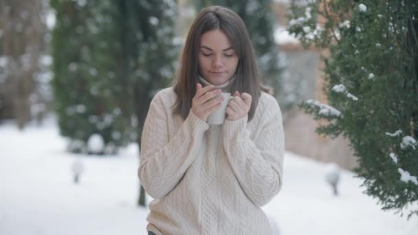 Porträtt av vacker ung brunett kvinna dricka te eller kaffe på vinterdagen utomhus. Mellanslag av leende avslappnad vit dam i tröja njuter av varm dryck. Livsstil och kallt väder. — Stockvideo