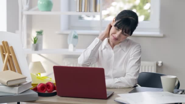 Portrait of sad slim beautiful businesswoman having pain in neck sitting in front of laptop at table. Young Caucasian brunette woman stretching muscles working in office. Sedentary lifestyle problems. — Stock Video