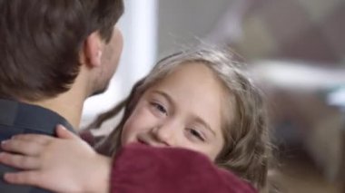 Kameraya bakıp gülümseyen, sarılan küçük güzel bir kızın yakından çekilmiş yüzü. Evde babasına sevgisini ifade eden mutlu beyaz bir kızın portresi. Aile bağı ve birlik.