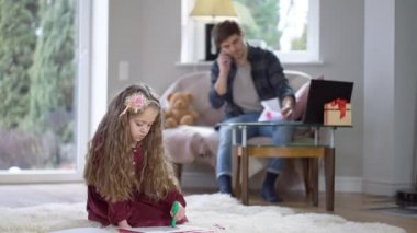 Güzel kıvırcık saçlı esmer kız arka planda telefonla konuşan bulanık bir adamla evde resim çiziyor. Babası tarafından göz ardı edilen beyaz bir kızın portresi..