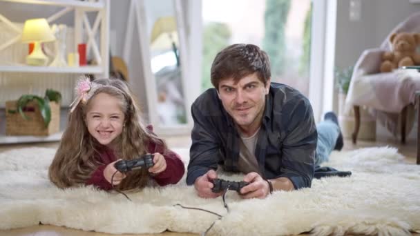 Alegre padre e hija usando consolas de juegos jugando videojuegos en casa los fines de semana. Retrato de niña caucásica emocionada absorbida ganando y hombre perdiendo. Tiempo libre y unidad familiar. — Vídeo de stock