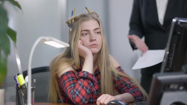 Portrait of bored arogan young woman sitting in office grimacing as unrecognizable boss gesturing showing documents at background. Milenial Kaukasia kasar membuat wajah mendengarkan CEO di kantor. — Stok Video