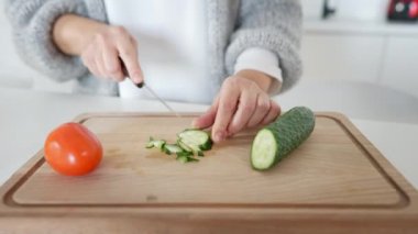 Mutfakta salatalık kesen beyaz kadın elleri kesme tahtasında. Ev içinde sağlıklı vejetaryen salatası pişiren tanınmayan orta yaşlı bir kadının yakın çekimi. Sağlıklı gıda konsepti.