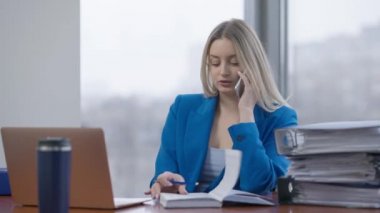 Yoğun özgüvenli iş kadınının portresi telefonda konuşuyor ve bilgisayardan mesajlaşıyor. Ofiste çalışan ince, sarışın, beyaz bir kadın. İş hayatı.