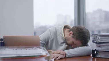 Genç, yorgun esmer adam ofiste uyuyor. Yorgun Kafkas erkek çalışanı iş yerinde kapalı yerde yatıyor. İş yorgunluğu ve yorgunluk kavramı.