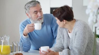 Rahatlamış yaşlı sakallı bir adamın portresi sabah kahvesini içip karısıyla mutfakta konuşuyor. Mutlu beyaz adam sarılıyor ve gülümsüyor. Aile birliği ve eğlence kavramı.