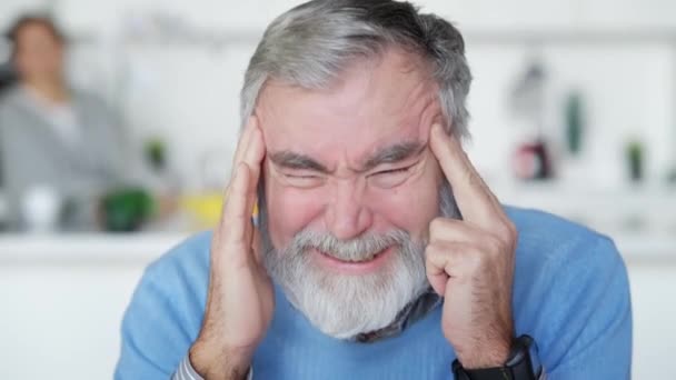 Zdjęcie smutnego, chorego starszego pana z silnym bólem głowy pocierającego skronie patrząc w kamerę. Portret białego emeryta z migreną w domu. Przewlekłe choroby i starzenie się. — Wideo stockowe