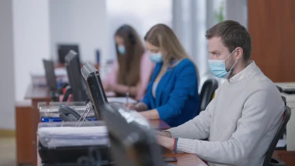 Kapalı mekanda çalışan Covid maskeli, konsantre ofis çalışanlarına odaklan. Koronavirüs salgınında bilgisayar kullanarak internetten mesajlaşan Kafkasyalı genç adam ve kadınlar. Covid-19 işi.