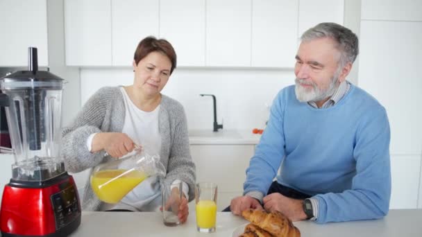 积极的老年男女早上在厨房倒橙汁喝。快乐轻松的白种人夫妇退休后在家里享受着健康的饮料. — 图库视频影像