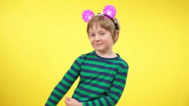 Sarı arka planda oyuncak fare kulağı takan neşeli küçük çocuğun komik dansı. Kameraya bakıp dans eden ve gülümseyen beyaz çocuk portresi. Eğlenceli konsept.