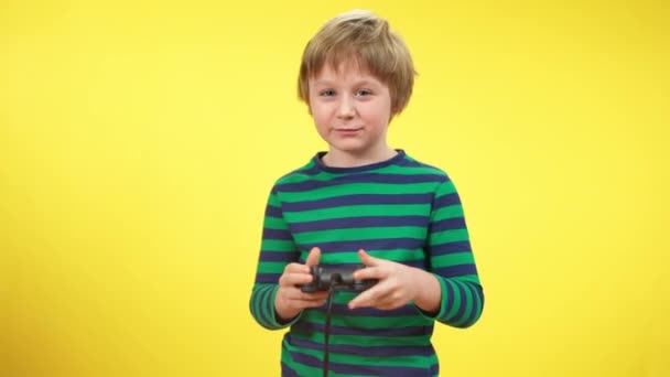 Aufgeregtes Kind spielt Spielkonsole und macht Siegesgeste vor gelbem Hintergrund. Porträt eines glücklichen unbeschwerten kaukasischen Jungen, der den Gewinn eines Videospiels genießt. Freizeit und Aufregung in der Kindheit. — Stockvideo