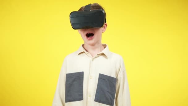 Blanke jongen in VR-headset schreeuwend tegen gele achtergrond. Midden schot van opgewonden kind met behulp van augmented reality voor gaming. Jeugd- en vrijetijdsconcept. — Stockvideo