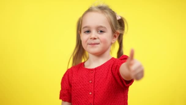 Fille souriante confiante montrant pouce vers le haut en regardant la caméra. portrait d'enfant caucasien joyeux posant sur fond jaune. Concept de bonheur et d'approbation. — Video