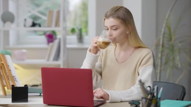 中间的照片是一个自信漂亮的高加索女人在网上发短信，在室内喝早茶。瘦小而集中的年轻女士在家网上工作的画像。信心概念. — 图库视频影像