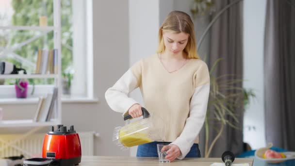 Střední záběr štíhlé nádherné mladé ženy, jak nalévá ovocný koktejl do skla a pije zdravý vitaminový nápoj. Portrét fit kavkazské krásné dámy těší chutný zdravý koktejl doma. — Stock video