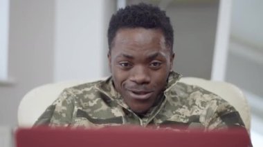 Neşeli, yakışıklı Afro-Amerikan askerinin yakın plan portresi. Görüntülü konuşma, jest ve gülümseme. Mutlu, gevşemiş bir askerin internette dizüstü bilgisayarla mesajlaşması. Yaşam tarzı kavramı.