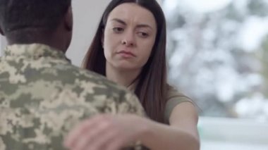 Kapalı alanda kamuflaj üniformalı Afro-Amerikalı bir adama sarılan üzgün, beyaz bir kadının yakın plan portresi. Duygusal güzel eş kocasını savaşa giderken görür. Aşk ve askerlik.
