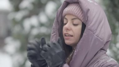 Dışarıda nefes alan deri eldivenlerle elleri ısıtan genç ve güzel bir kadının yakın çekimi. Kendine güvenen beyaz çağının portresi kar yağarken kış tatilinin tadını çıkarıyor..