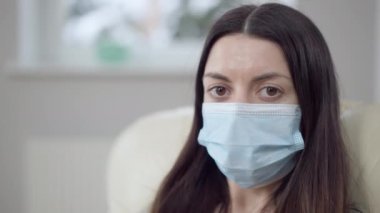 Covid maskesiyle kameraya bakan üzgün, hasta genç bir kadının vesikalığı. Coronavirus salgını belirtileri gösteren güzel beyaz kadın portresi..