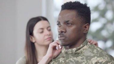 Düşünceli Afro-Amerikan askerinin yakın plan portresi bulanık beyaz kadın üniformasını düzeltiyor. Evde kendine güvenen asker ve gururlu eş.