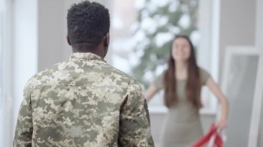 Arka planda ulusal bayrağı sallayan Afrikalı Amerikalı genç adamın bulanık, beyaz bir kadınla el ele tutuşması. Erkek asker eve dönüyor. Mutlu evlilik ve kavuşma.