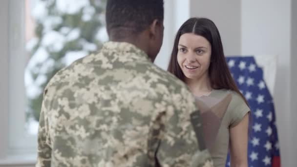 Retrato de mujer hermosa feliz que recibe ramo de flores del hombre y abrazo amante cónyuge. Sorprendido esposa caucásica abrazando marido afroamericano en casa con la bandera de EE.UU. en el fondo. — Vídeos de Stock