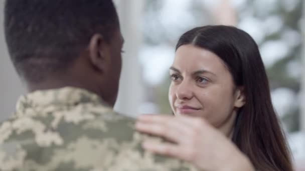 Primer plano de encantadora mujer caucásica cariñosa y afectuoso hombre afroamericano en uniforme militar bailando en casa. Feliz pareja interracial relajada disfrutando de la reunión en interiores. — Vídeos de Stock