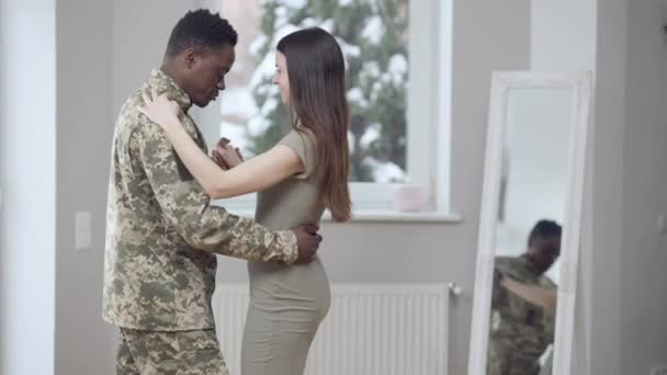 Älskar glada interracial unga par valsar inomhus leende. Porträtt av romantisk afroamerikansk militär man och vacker smal vit kvinna som dansar hemma. Kärlek och återförening koncept. — Stockvideo