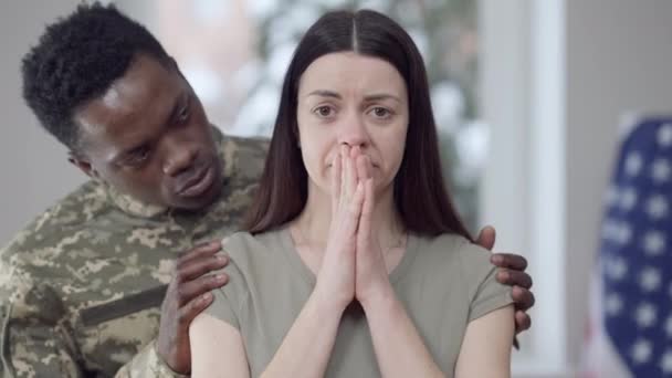 Porträtt av gråtande ung vacker vit kvinna med afroamerikansk militär man lugnande ner make. Tråkig olycklig fru hemma med man som ger sig ut i krig. Familje- och försvarsindustrin. — Stockvideo