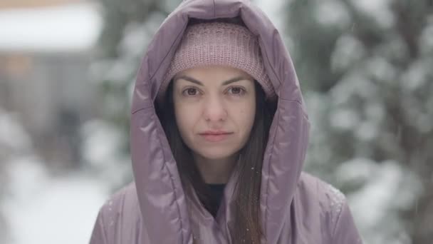 Közelkép bájos barna nő barna szeme áll a hóesésben nézi a kamerát. Gyönyörű fiatal kaukázusi hölgy pózol a szabadban a havas téli napon. Hideg időjárás koncepciója. — Stock videók