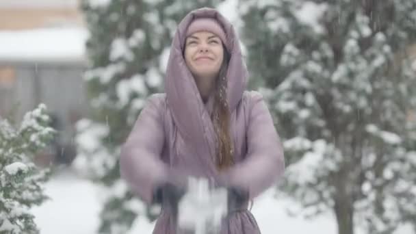 喜びのスリムな若い女性が屋外で笑みを浮かべて雪を投げる。雪の冬の日に屋外で楽しんでいる美しいコーカサスのブルネットの女性の肖像画。幸福とレジャーの概念. — ストック動画