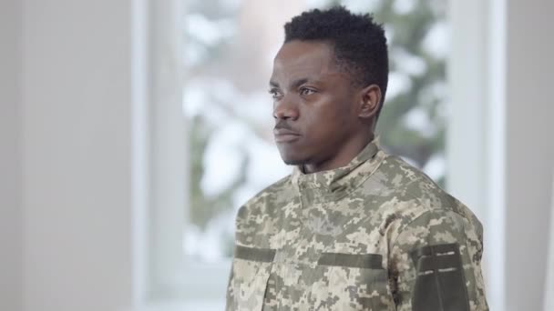 Joven recluta guapo girando a la cámara y saludando en el interior. Retrato de un hombre valiente afroamericano confiado en uniforme militar mirando a la cámara con expresión facial seria. Deber y estilo de vida — Vídeos de Stock