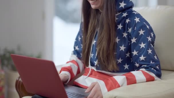 Glädjande oigenkännlig ung kvinna som ler och vinkar i videochatt. Glad avslappnad kaukasisk tusenårig i huvtröja meddelanden online på laptop sitter på fåtölj hemma. — Stockvideo