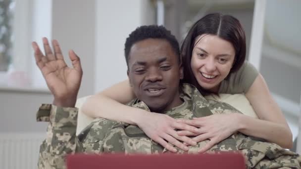 Portrait de heureux couple interracial messagerie en ligne en utilisant le chat vidéo sur ordinateur portable. Homme afro-américain souriant positif et femme caucasienne agitant et parlant se reposant à la maison à l'intérieur. Mode de vie. — Video