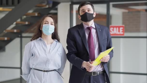 Client and broker in coronavirus face masks talking gesturing and shaking hands standing in new premises indoors. Portrait of confident Caucasian woman and man in new flat on Covid pandemic. — Stock Video