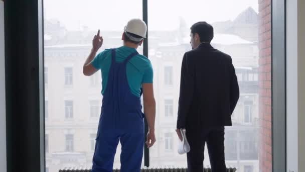 Jeune constructeur confiant et acheteur serrant la main debout à la fenêtre à l'intérieur. Vue arrière de l'homme de service caucasien professionnel et propriétaire de locaux faisant affaire dans un appartement ou un bureau neuf. Réparation rénovation. — Video