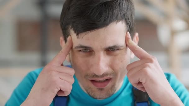 Kopfschuss-Porträt eines jungen kaukasischen Servicemanns, der drinnen unter starken Kopfschmerzen leidet. Großaufnahme des traurigen gestressten Bauarbeiters in Uniform mit Schmerzen im Kopf. Migräne und Gesundheitsfürsorge. — Stockvideo