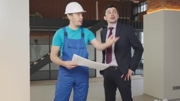 Builder and house owner discussing repair renovation indoors. Portrait of positive handsome Caucasian men talking and examining plan in new flat. Real estate ownership and service concept. — Stock Video