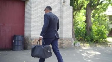 Kamera Afro-Amerikalı işadamını takip ediyor. Çantasıyla terk edilmiş varoşlara yürüyor ve büyük kırmızı ahşap kapıyı çalıyor. Açık havada güneşli bir günde kaba ve başarılı bir adam görüntüsü..