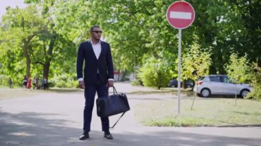 Güneşli bir günde elinde çantasıyla dışarıda duran kendine güvenen Afro-Amerikan bir adamın geniş açılı portresi. Şehir parkında buluşmayı bekleyen başarılı yakışıklı adam. Turizm ve iş.