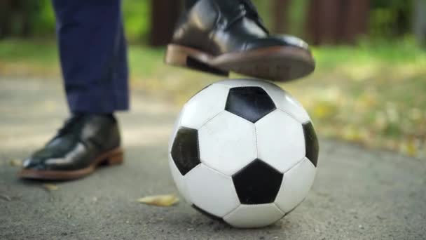 Detailní záběr mužská noha v elegantní kožené botě krok na fotbalový míč venku. Neznámý stylový podnikatel s fotbalovým vybavením v parku. Životní styl a koníček. — Stock video