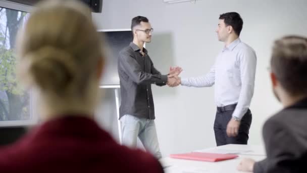 Socios de negocios exitosos estrechando la mano en la sala de reuniones con gente borrosa aplaudiendo. Hombres caucásicos seguros haciendo tratos en el cargo. Asociación y cooperación. — Vídeo de stock