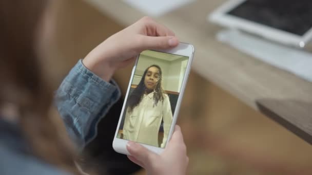 Экран смартфона с веселыми афроамериканками разговаривают. Неузнаваемая кавказская школьница держит в руках гаджет, общаясь онлайн с одноклассницей. Современный стиль. — стоковое видео