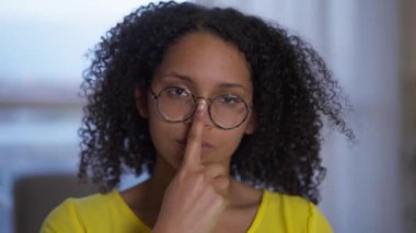 Gözlüklü Afro-Amerikan kadının kameraya bakan özgüvenli portresi. Coronavirus tecridiyle ilgili ofis içinde poz veren güzel, genç ve zeki bir serbest yazar..