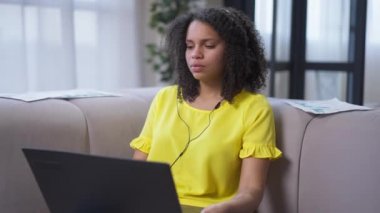 Kulaklıklı akıllı Afro-Amerikan kadın diz üstü bilgisayarı kapatıp kameraya bakıp gülümsüyor. Evden salgın hastalıklar üzerinde çalışan kendinden emin, serbest çalışan birinin portresi. Yeni normal yaşam tarzı.