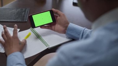 Kromakey yeşil ekranlı akıllı telefonu tutan tanınmamış Afrikalı Amerikalı adam. Genç ve düşünceli bir işadamı ev ofisindeki e-market planlama işini inceliyor..