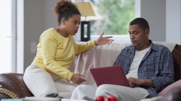 Irritált afro-amerikai feleség vitatkozik abszorbeált férjjel, aki a laptopon üzenget. Problémák a távoli munkavégzéssel az otthoni irodában a koronavírus lezárásán. Konfliktus és szabadúszó koncepció. — Stock videók