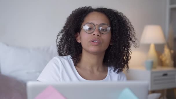 Vooraanzicht portret van zelfverzekerde mooie Afro-Amerikaanse jonge vrouw in bril praten met behulp van virtuele conferentie over pandemische lockdown. Slimme succesvolle freelancer die online werkt vanuit huis. — Stockvideo