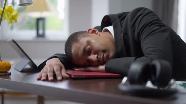 Uomini afroamericani esausti che dormono su un computer portatile in un ufficio al chiuso. Ritratto di giovane e stanco bel ragazzo disteso a tavola in salotto con gli occhi chiusi. Burnout sul lavoro a distanza. — Video Stock