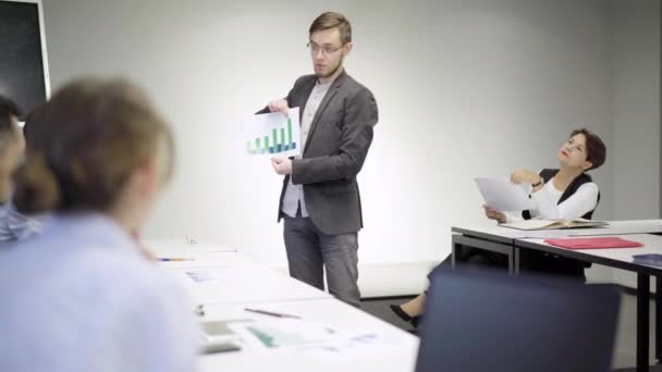 Portret van een glimlachende, zelfverzekerde jongeman die een businessplan presenteert voor collega 's. Positief succesvolle blanke werknemer bespreken startup project met collega 's binnen. Teamwork concept. — Stockvideo